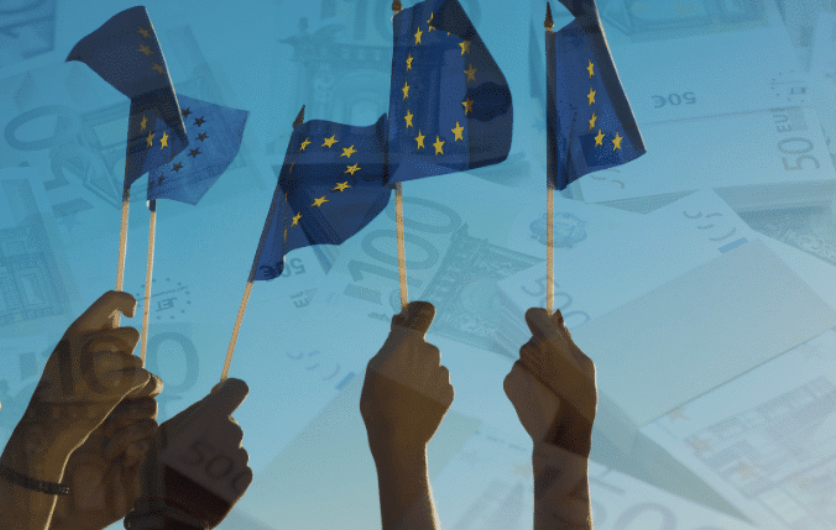 Hands raising small European Union flags over a background of euro banknotes